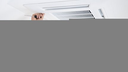 Ein Mann mit Vollbart hält ein Lüftungsgitter an der Decke