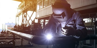 Ein Anlagenmechaniker der an einer Werkbank ein Rohr mit einem Winkelschleifer bearbeitet